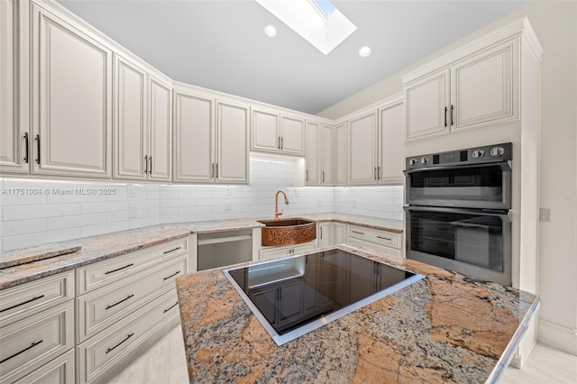 kitchen featuring light stone countertops, a skylight, a sink, appliances with stainless steel finishes, and decorative backsplash