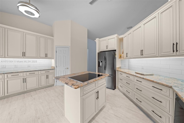 kitchen featuring tasteful backsplash, stainless steel fridge with ice dispenser, a kitchen island, light stone countertops, and black electric stovetop