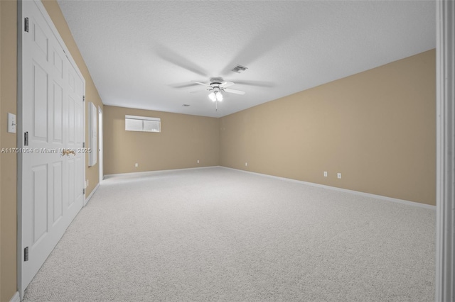 spare room featuring a textured ceiling, light colored carpet, visible vents, baseboards, and a ceiling fan