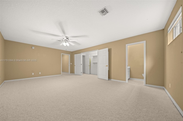 unfurnished bedroom with a textured ceiling, connected bathroom, light colored carpet, visible vents, and baseboards