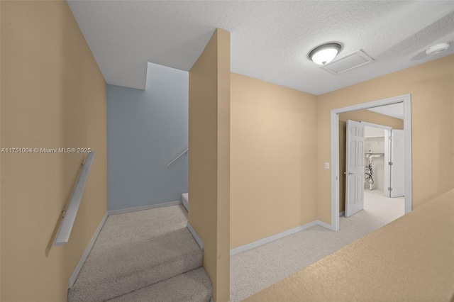 hall featuring baseboards, visible vents, light carpet, and a textured ceiling