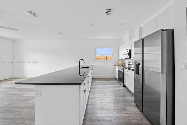 kitchen featuring visible vents, white cabinets, appliances with stainless steel finishes, a center island, and dark countertops