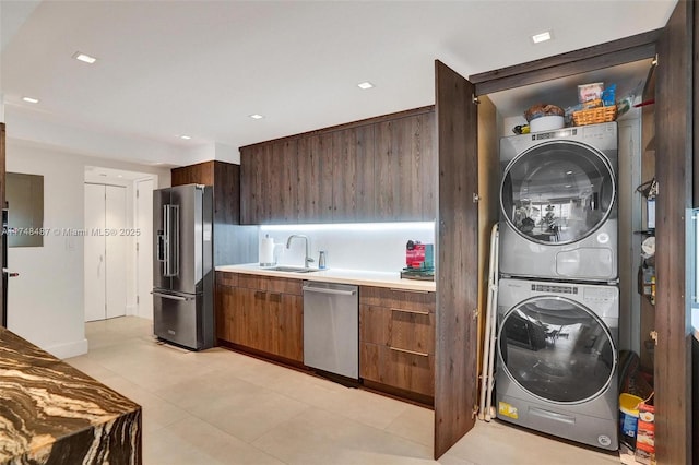 kitchen featuring stainless steel appliances, stacked washer / dryer, a sink, light countertops, and modern cabinets