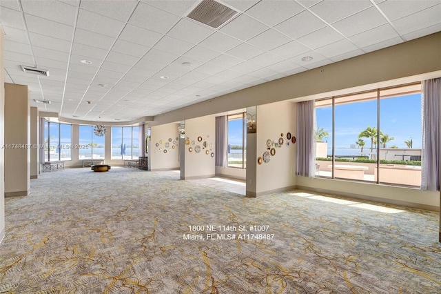 unfurnished living room featuring a healthy amount of sunlight, visible vents, and a drop ceiling