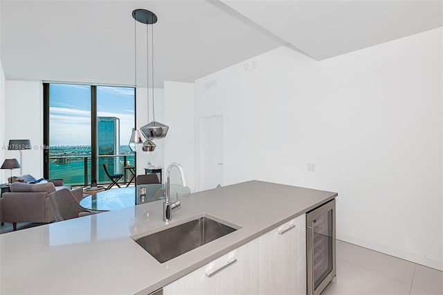 kitchen featuring wine cooler, open floor plan, light countertops, pendant lighting, and a sink