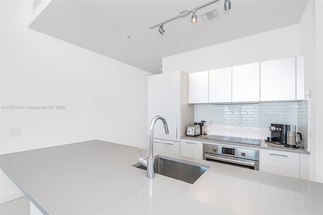 kitchen featuring white cabinetry, stainless steel oven, a sink, modern cabinets, and black electric cooktop