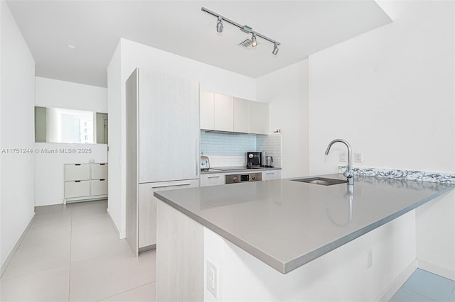 kitchen featuring a peninsula, tasteful backsplash, light tile patterned flooring, and a sink