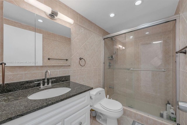 full bath with a stall shower, tile walls, toilet, and vanity