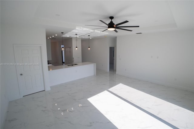 unfurnished living room featuring baseboards, a raised ceiling, marble finish floor, a sink, and recessed lighting