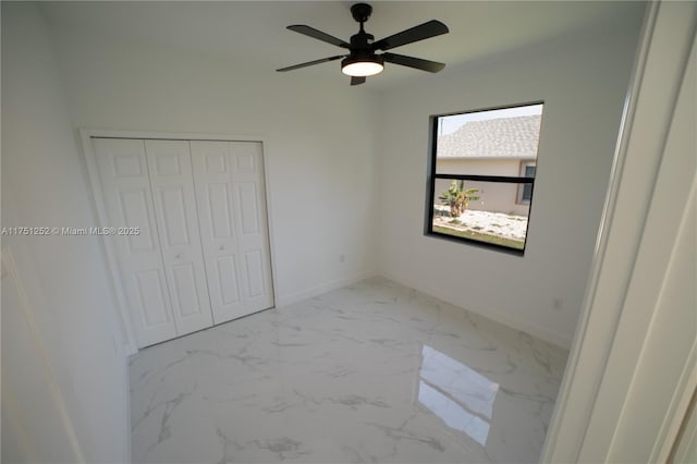 unfurnished bedroom featuring a closet, marble finish floor, baseboards, and a ceiling fan