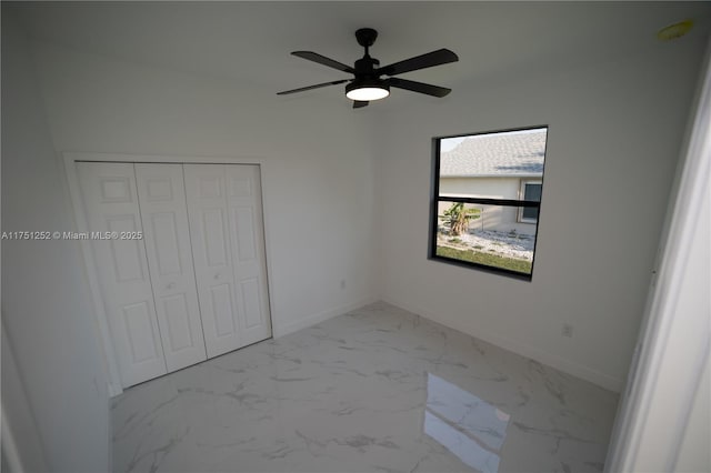 unfurnished bedroom with a closet, marble finish floor, baseboards, and a ceiling fan