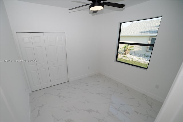 unfurnished bedroom featuring marble finish floor, ceiling fan, baseboards, and a closet