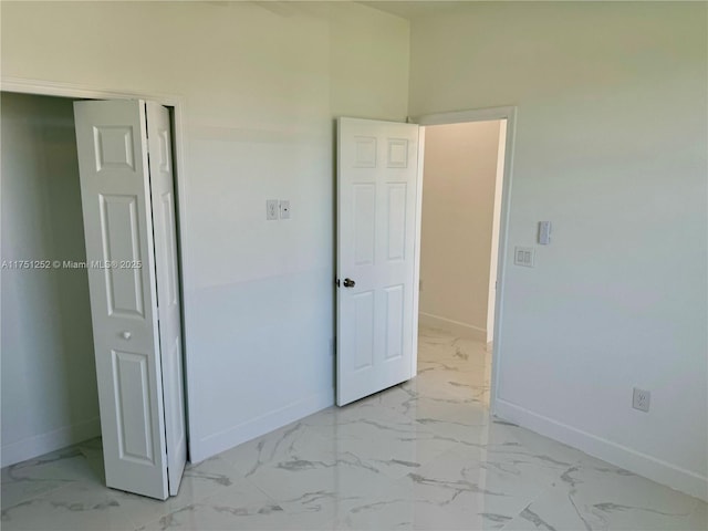 unfurnished bedroom with a closet, marble finish floor, and baseboards