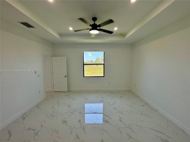 empty room with a tray ceiling, marble finish floor, visible vents, and baseboards