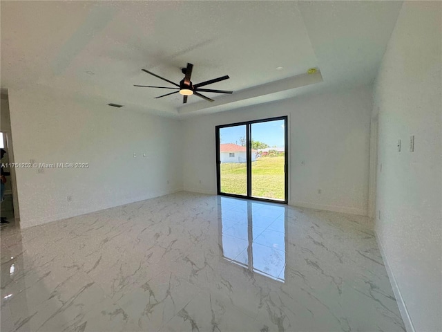 spare room with a ceiling fan, a tray ceiling, marble finish floor, and baseboards