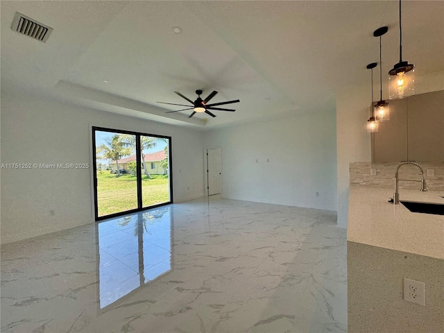 empty room with a tray ceiling, marble finish floor, visible vents, a sink, and ceiling fan