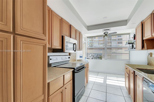 kitchen with light tile patterned floors, stainless steel appliances, a ceiling fan, brown cabinetry, and a raised ceiling