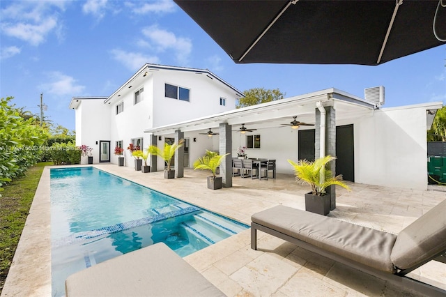 rear view of property with ceiling fan, a patio, outdoor dining area, a pool with connected hot tub, and stucco siding