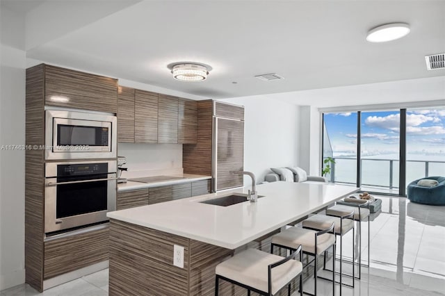 kitchen featuring a breakfast bar area, a sink, stainless steel appliances, light countertops, and brown cabinets