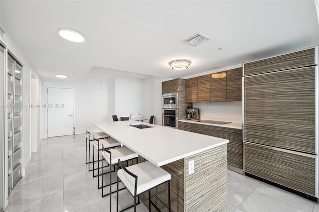 kitchen featuring light tile patterned floors, visible vents, a breakfast bar, a sink, and stainless steel appliances