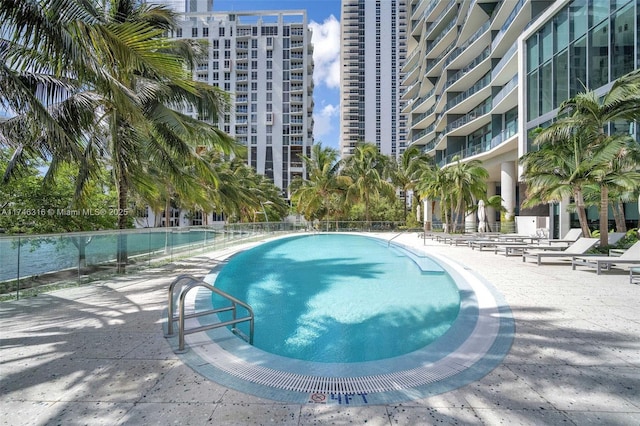 pool with a patio, a view of city, and fence