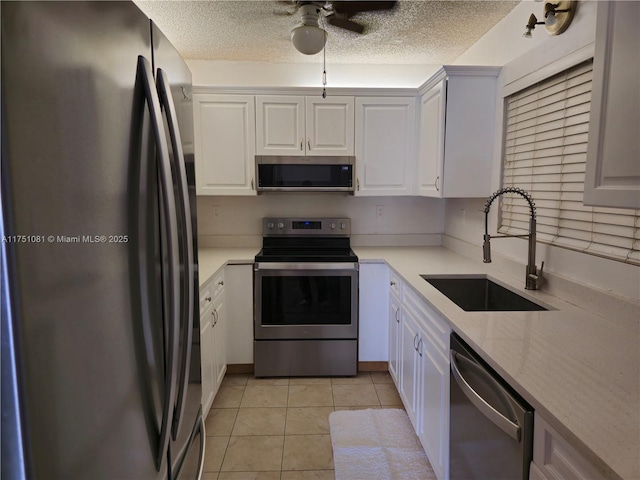 kitchen with a textured ceiling, appliances with stainless steel finishes, a sink, and light tile patterned flooring