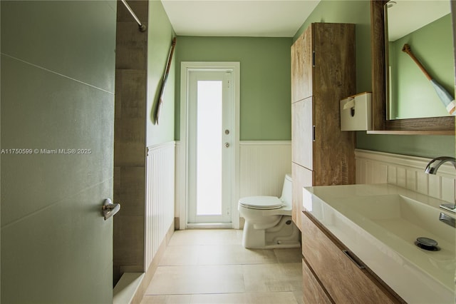 full bath featuring tile patterned flooring, wainscoting, vanity, and toilet