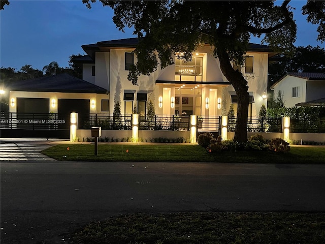 property at night featuring a garage, a fenced front yard, and driveway
