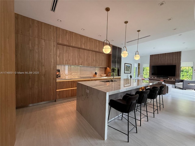 kitchen with a large island, modern cabinets, light wood-type flooring, brown cabinetry, and light stone counters