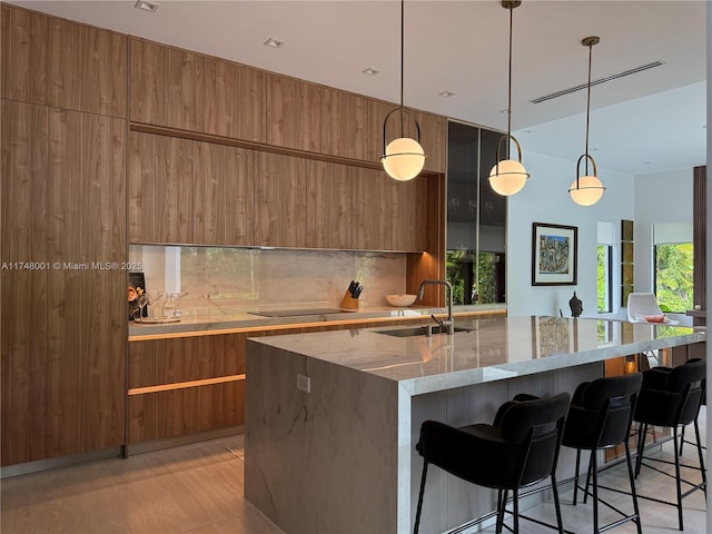 kitchen featuring modern cabinets, brown cabinetry, a kitchen bar, light stone counters, and backsplash