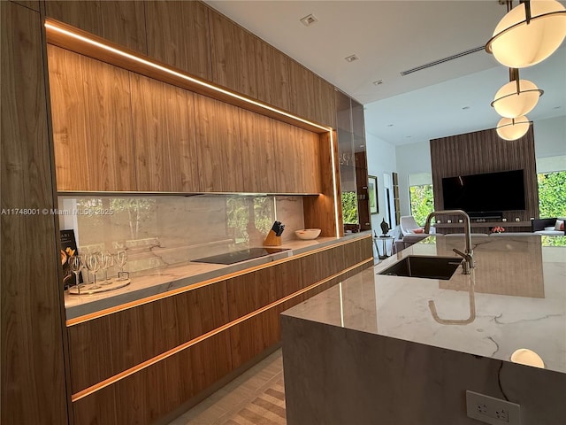 kitchen featuring black electric cooktop, modern cabinets, a sink, open floor plan, and light stone counters
