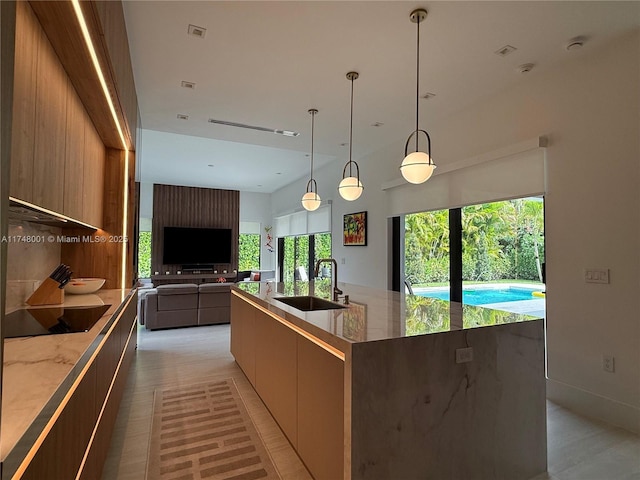 kitchen featuring modern cabinets, light stone counters, a sink, open floor plan, and black electric stovetop