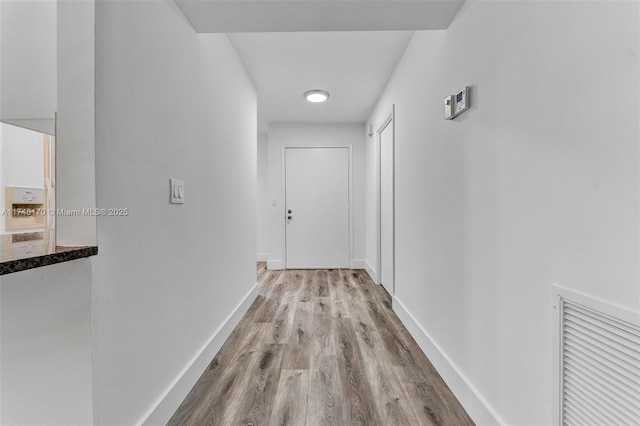 hallway featuring light wood finished floors, visible vents, and baseboards