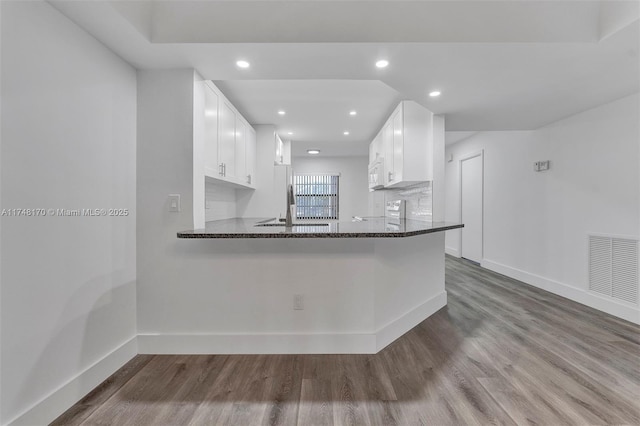 kitchen with visible vents, white cabinets, dark stone countertops, wood finished floors, and a peninsula