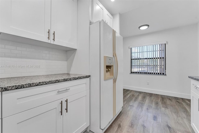 kitchen with light wood finished floors, white refrigerator with ice dispenser, baseboards, white cabinetry, and backsplash