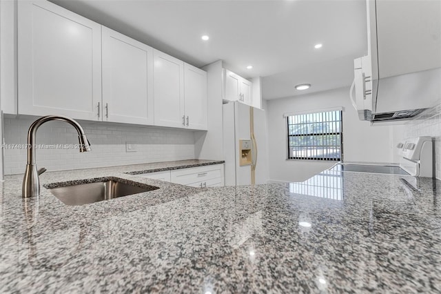 kitchen with light stone counters, white refrigerator with ice dispenser, stove, a sink, and white cabinetry