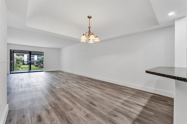 unfurnished dining area featuring wood finished floors, a chandelier, baseboards, a tray ceiling, and recessed lighting