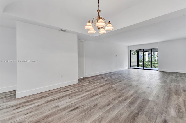 unfurnished room with visible vents, a notable chandelier, light wood-style flooring, and baseboards