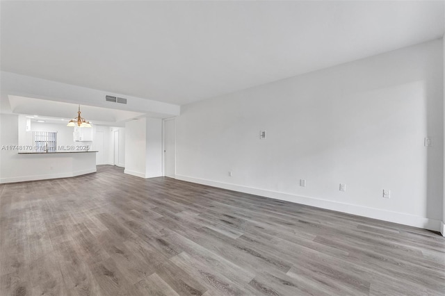 unfurnished living room featuring light wood-type flooring, visible vents, baseboards, and an inviting chandelier