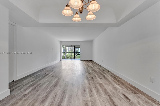 spare room with wood finished floors, a chandelier, baseboards, and a raised ceiling