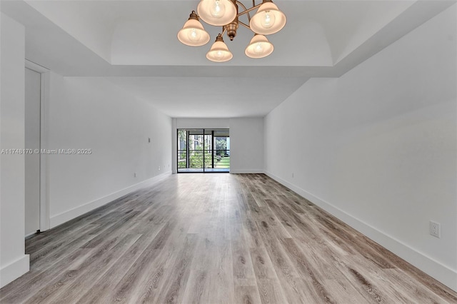 empty room featuring light wood-type flooring, baseboards, and a notable chandelier