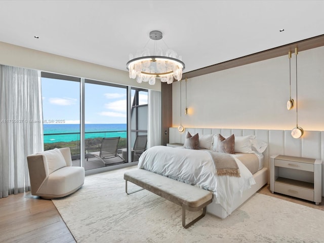 bedroom featuring light wood finished floors, a water view, an inviting chandelier, and access to exterior