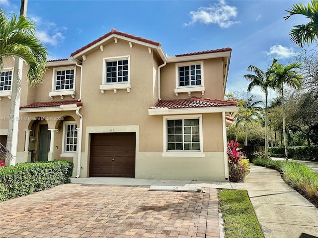 mediterranean / spanish house featuring an attached garage, a tiled roof, decorative driveway, and stucco siding