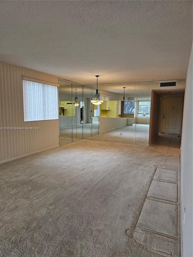 empty room with a textured ceiling, a wealth of natural light, carpet, and visible vents