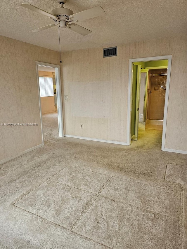 carpeted empty room with visible vents, ceiling fan, a textured ceiling, and baseboards