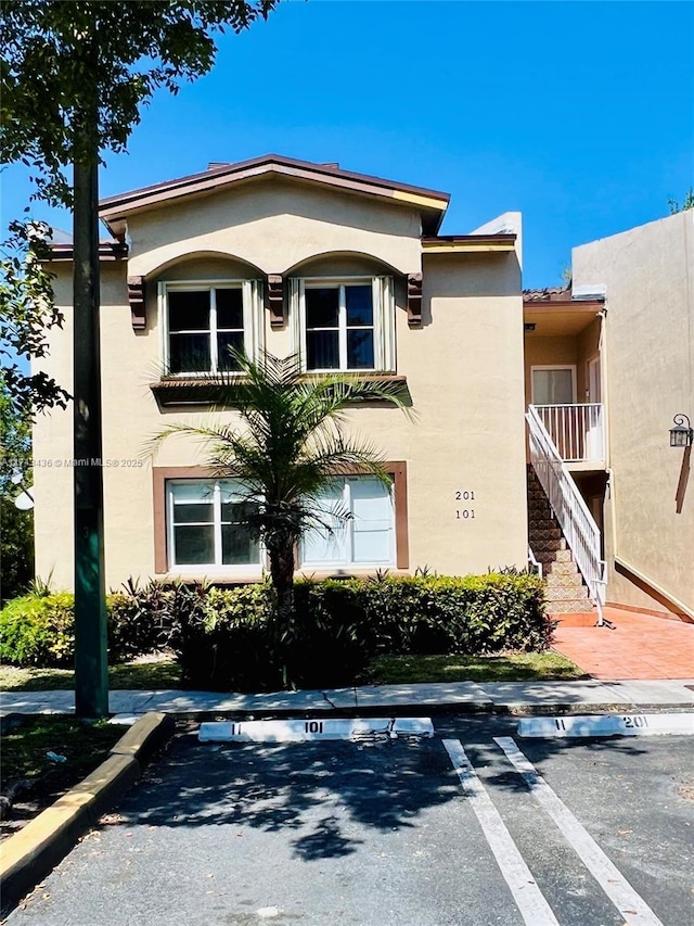 exterior space featuring stairs, uncovered parking, and stucco siding