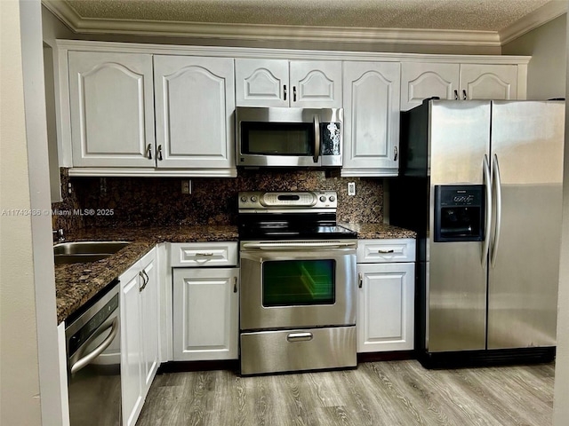 kitchen featuring stainless steel appliances, white cabinetry, decorative backsplash, light wood finished floors, and crown molding