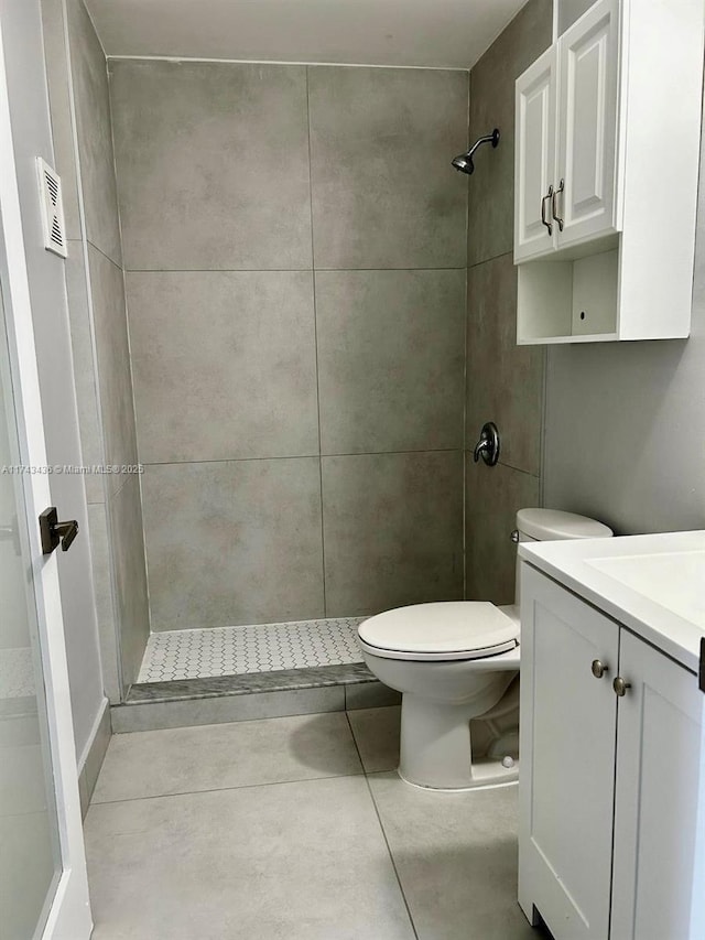 bathroom with visible vents, toilet, tile patterned floors, a tile shower, and vanity