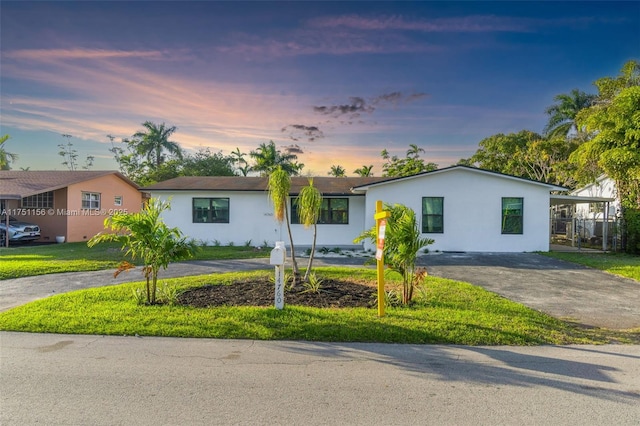 single story home with aphalt driveway, a lawn, and stucco siding