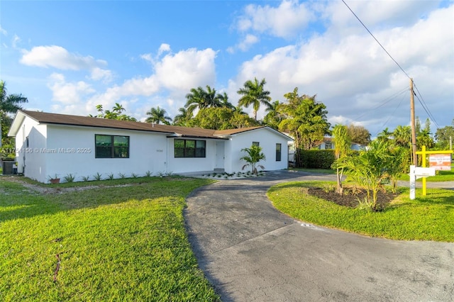 ranch-style home with central air condition unit, stucco siding, aphalt driveway, and a front yard